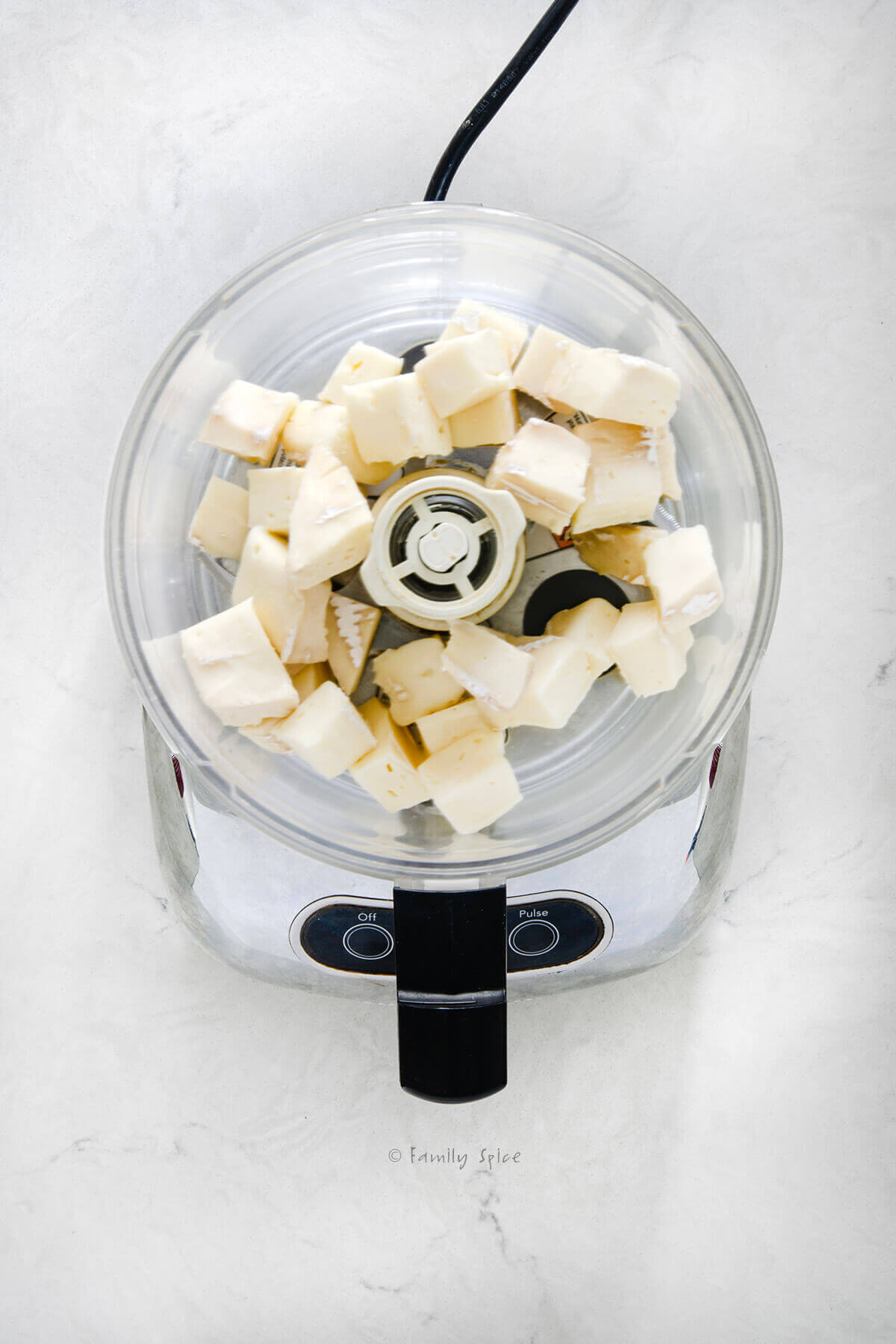 Top view of a food processor with cubed chunks of brie in it