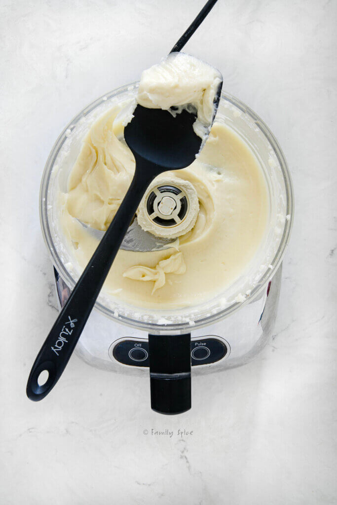 Top view of a food processor with the finished whipped brie in it and a silicone scraper on top with brie on it