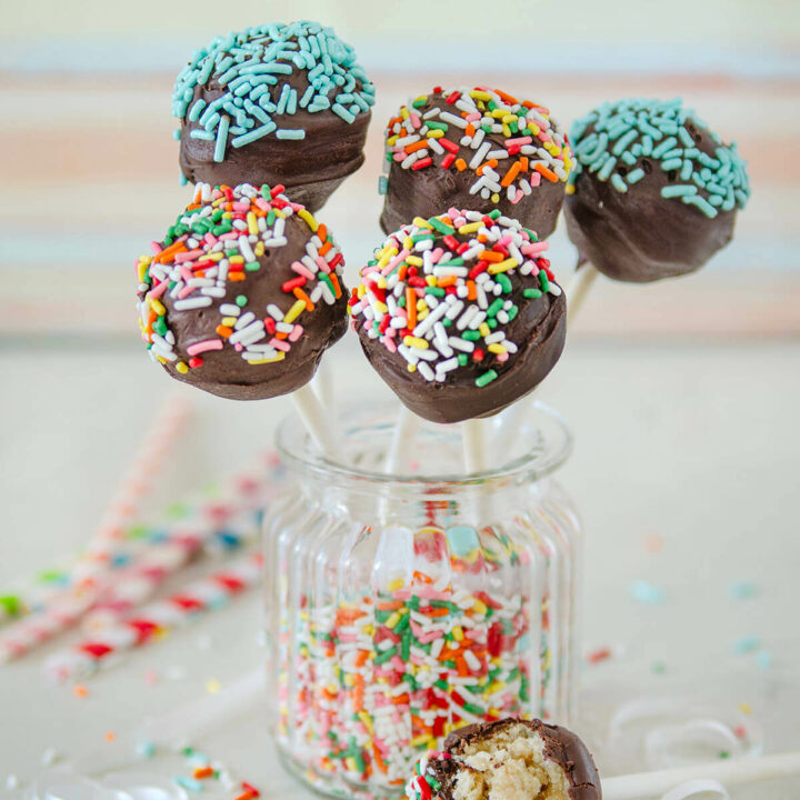 A jar filled with sprinkles and 5 vegan pops inserted in it