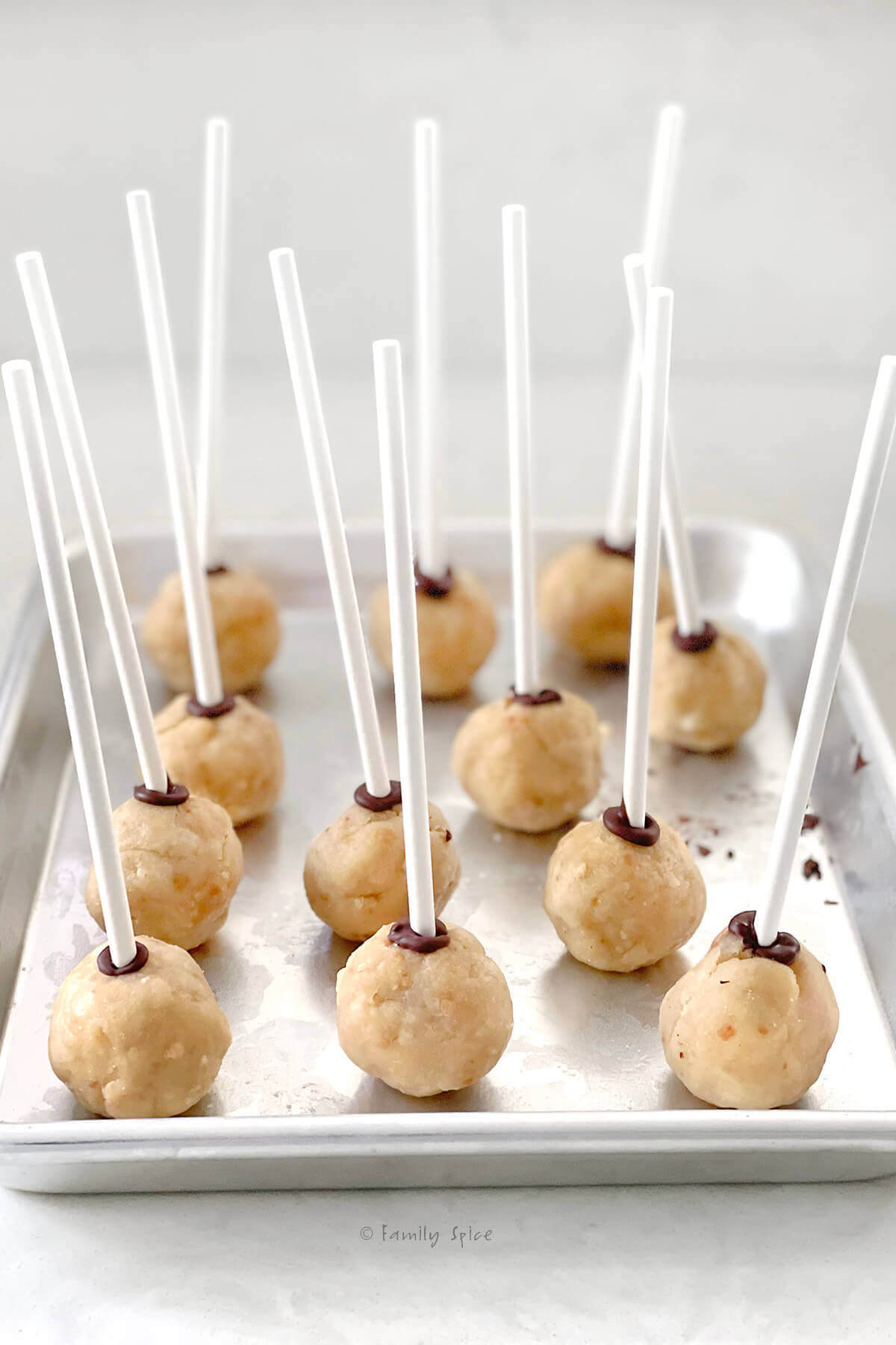 Side view of a small baking tray with cake pops with a lollipop stick inserted into it
