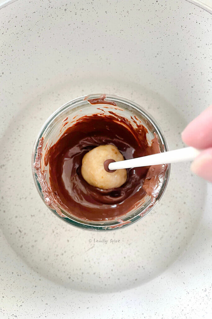 A hand dipping a vegan cake pop into a glass with melted chocolate in it