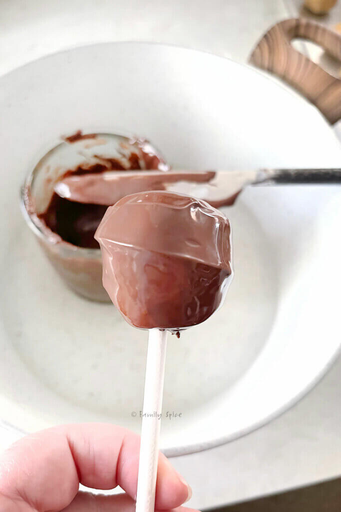 A hand holding a chocolate dipped cake pop and smoothed with a knife