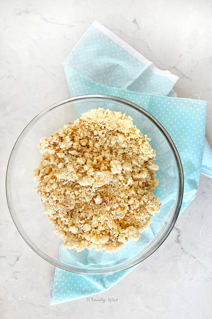 A glass mixing bowl with vegan cake crumbs on a light blue napkin