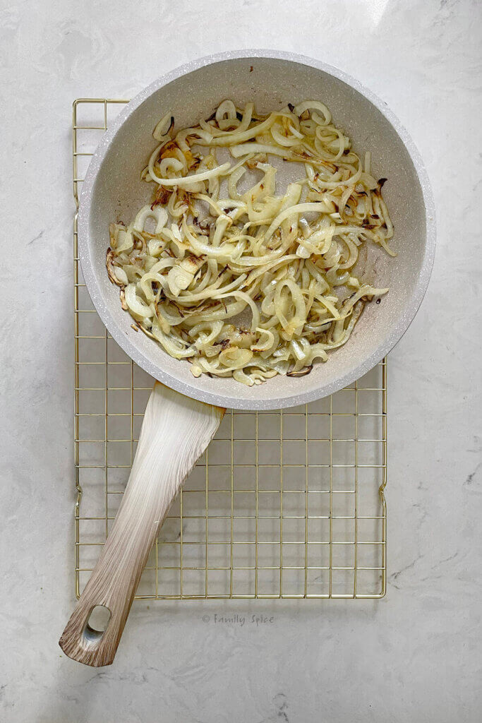 Top view of a light colored frying pan on a cooling rack with onion slices slowly getting browned