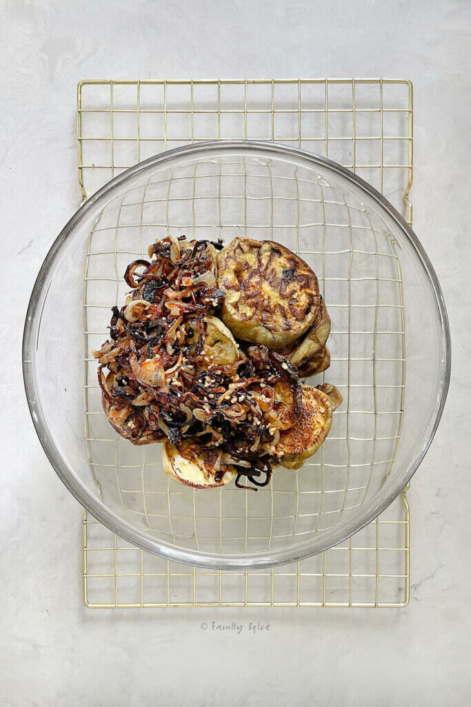 A glass mixing bowl on a cooling rack with caramelized onion slice and roasted eggplant slices in it