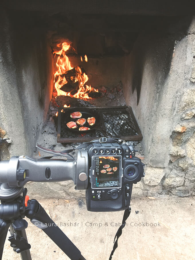 A camera on a tripod shooting pears cooking on a cast iron pan in an outdoor fireplace