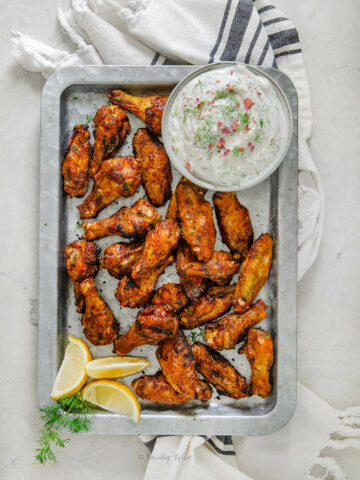 Top view of Persian chicken wings on a metail tray with lemon wedges and yogurt