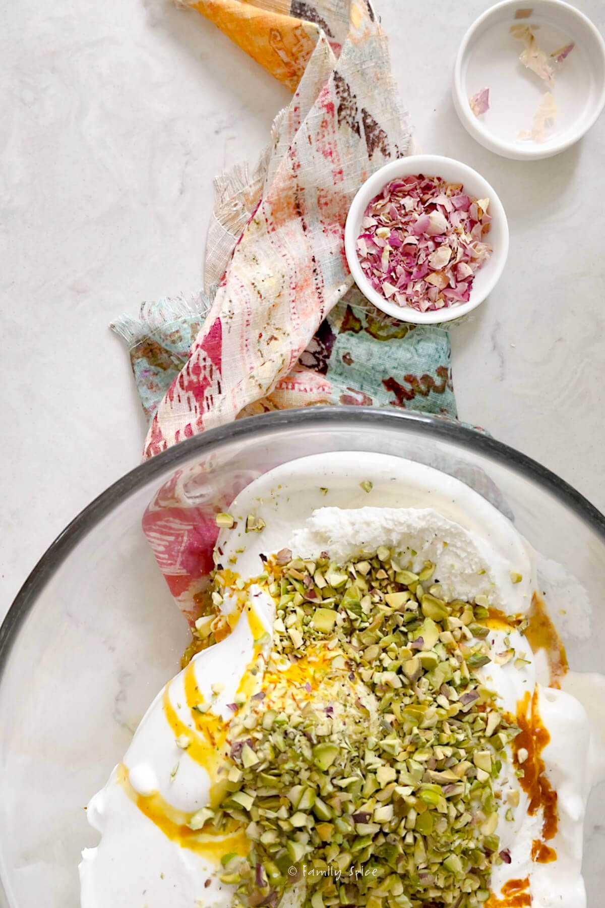 Top view of a large glass mixing bowl with melty vanilla ice cream topped with saffron water and chopped pistachios