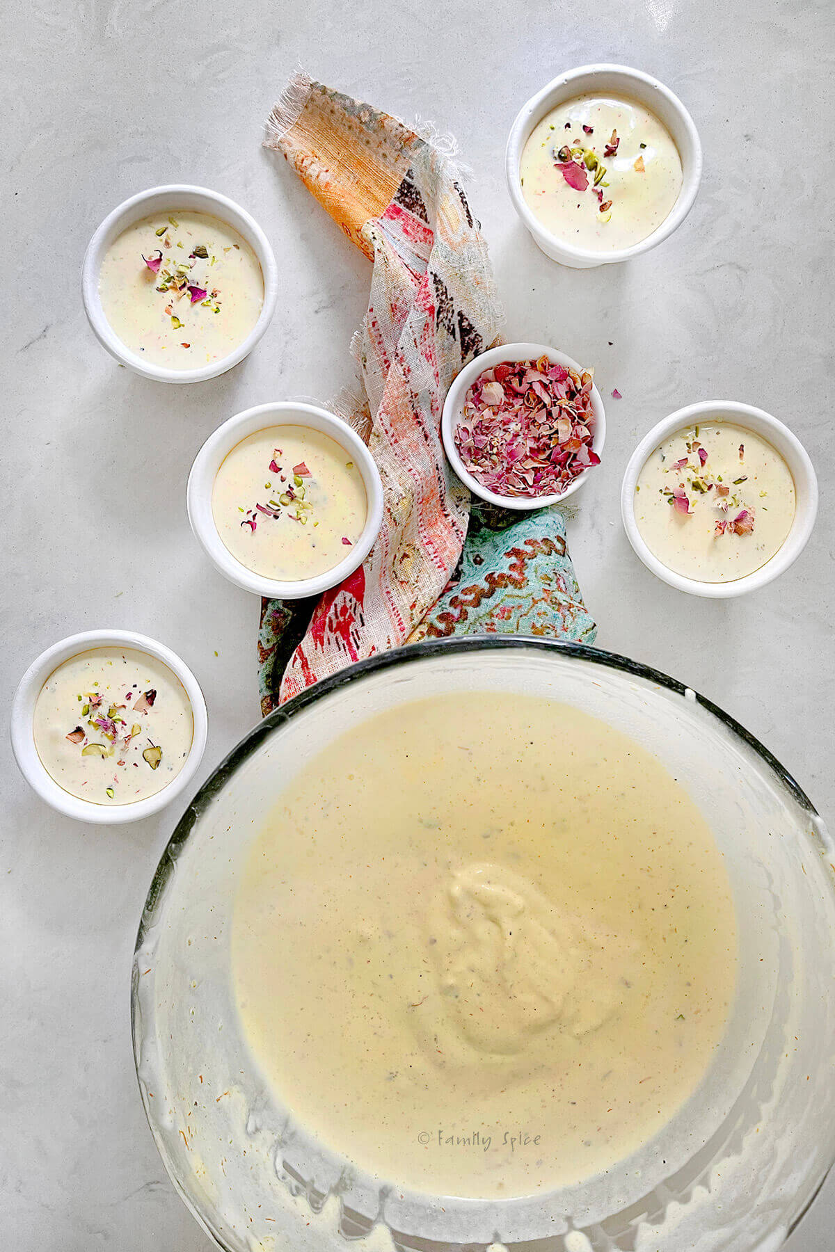 Top view of a large glass mixing bowl with melty saffron pistachio ice cream in it with small disposable bowls with the same ice cream in it