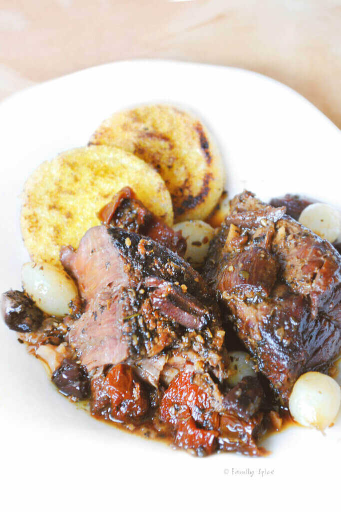 Closeup of Italian Pot Roast with polenta rounds on a white plate