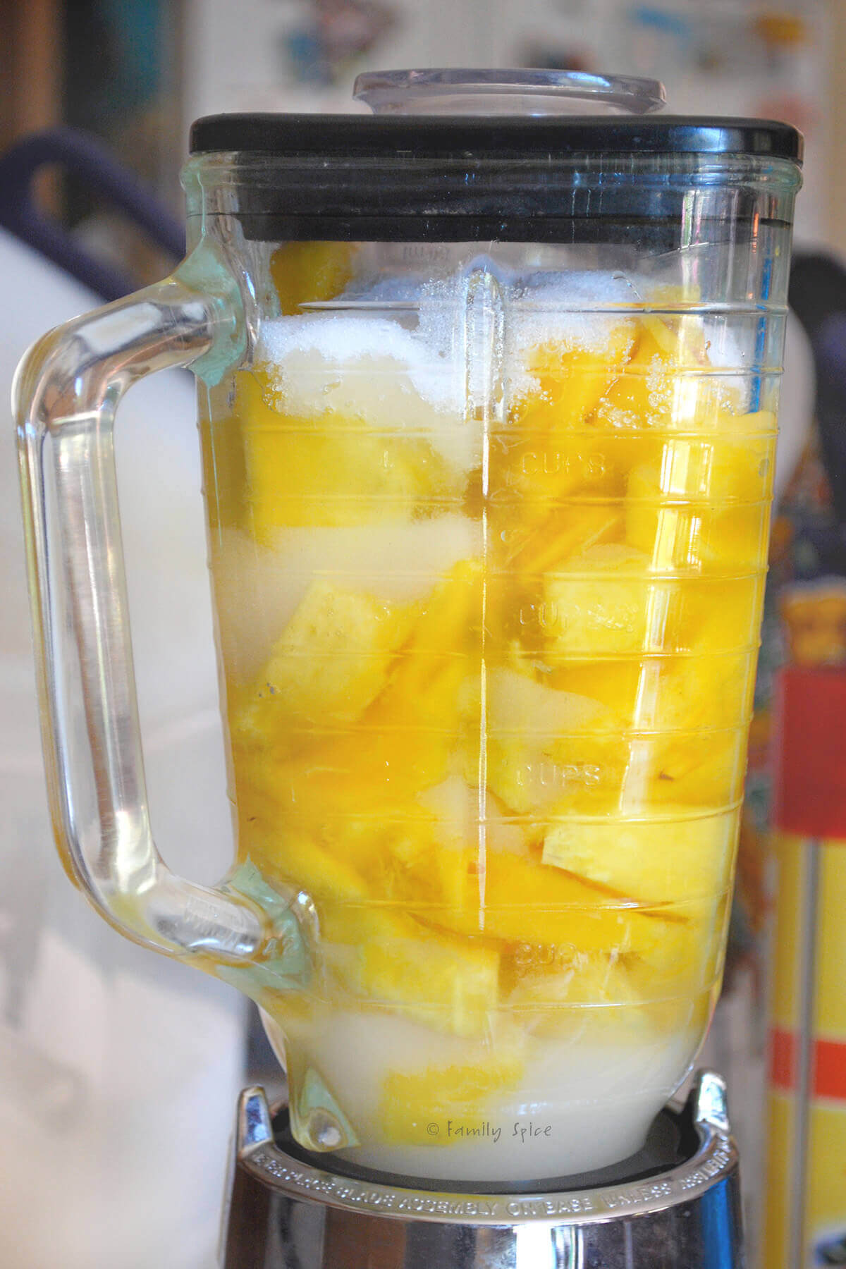 side view of a blender with chopped mango, sugar and lime juice in it