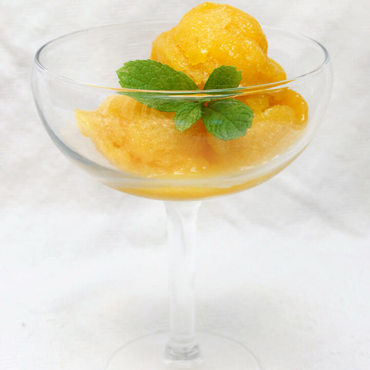 Side view of a stem glass with mango sorbet and a bit of fresh mint in it