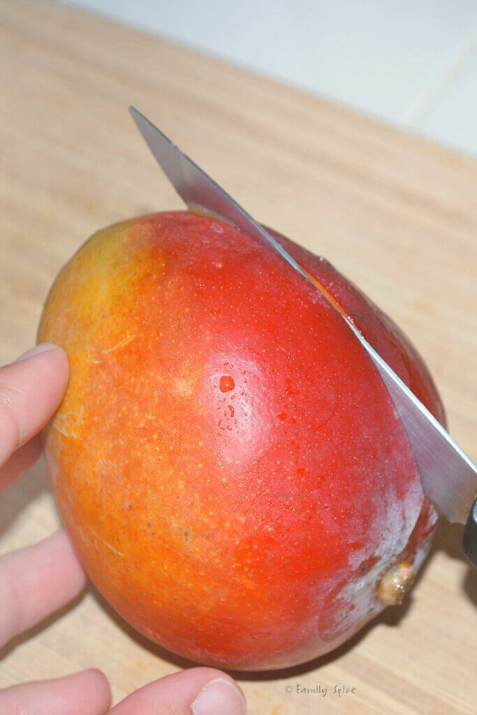 A hand holding a mango and a knife cutting into it