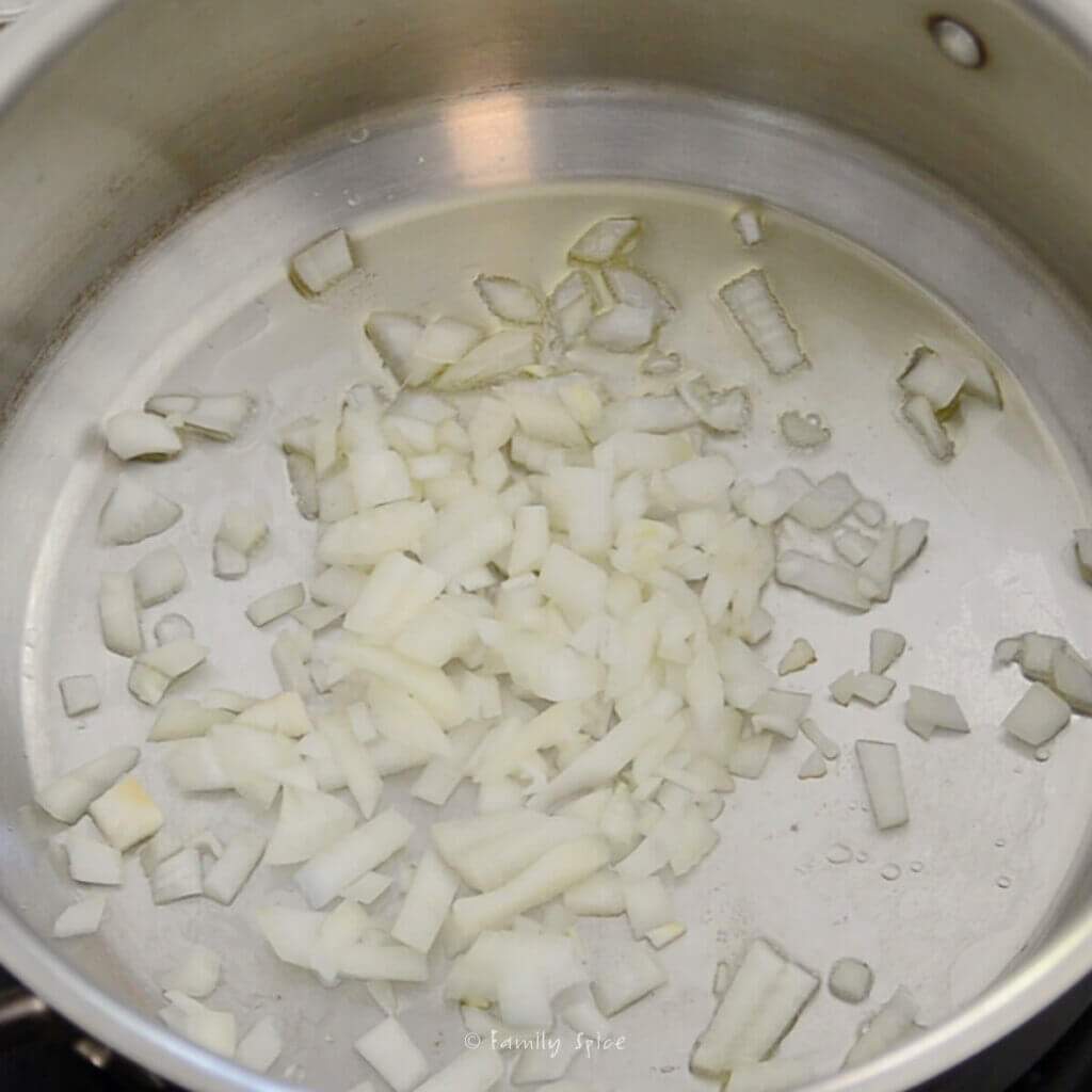 Chopped onions sautéing in hot oil in a stainless pot