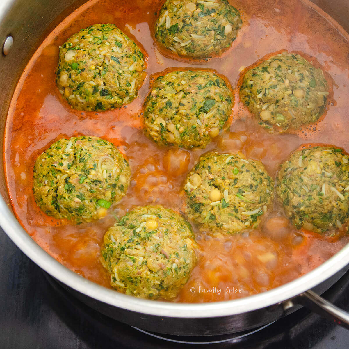 Raw Persian meatballs (koofteh berenji) added to hot tomato broth simmering in a stainless pot