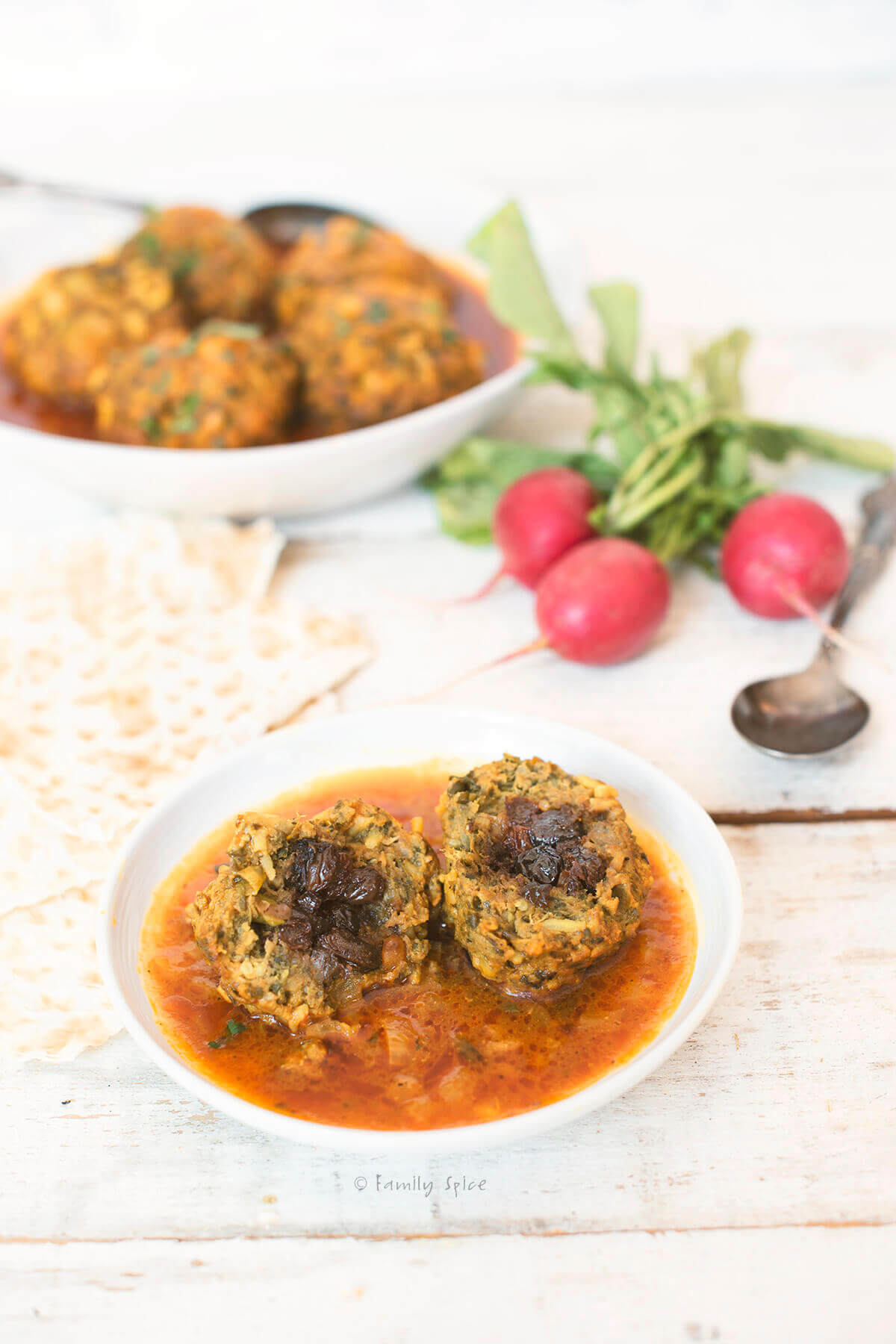 ¾ view of koofteh berenji with meatball cut open and a serving dish, radishes and lavash behind it
