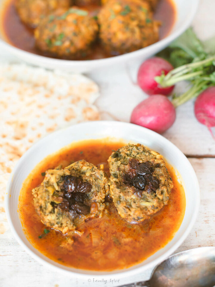 Closeup of koofteh berenji with meatball cut open and a serving dish, radishes and lavash behind it