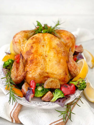 Side view of a whole roast chicken golden yellow from saffron with roasted vegetables around it on a white platter