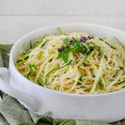 Side view of a white round casserole dish with pasta and zucchini topped with basil and grated parmesan