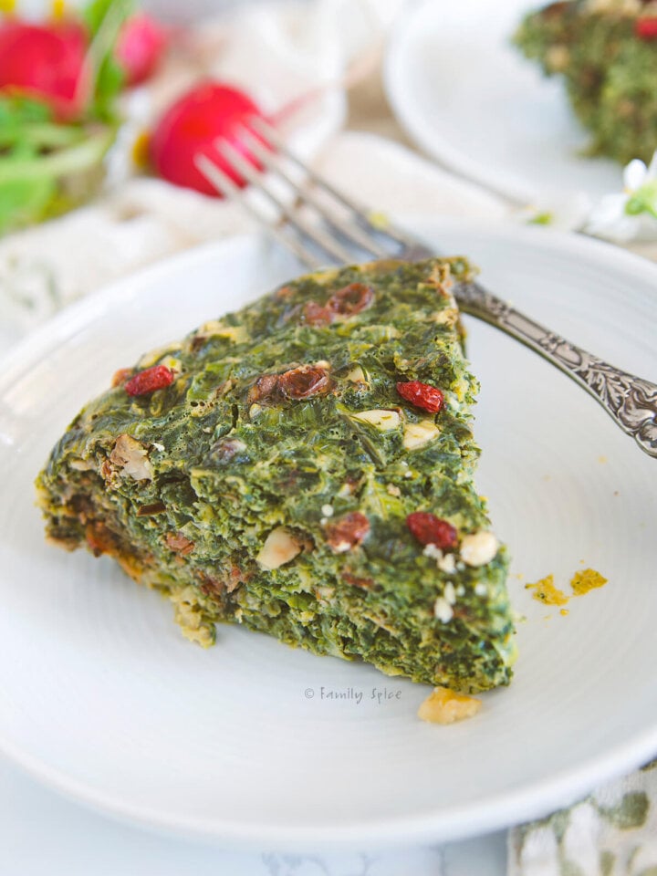 Closeup shot of a slice of kuku sabzi on a white plate with radishes by FamilySpice.c