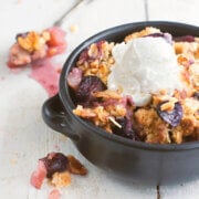 Closeup of a small black bowl with apple grape crisp in it and topped with a scoop of vanilla ice cream on it.