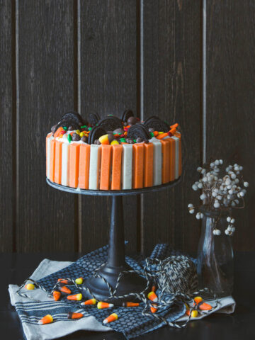 A halloween kit kat ice cream cake on a black cake pedestal with candies around it