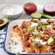 Side view of tachos topped with pulled pork, cheese, pico de gallo, sour cream and avocados.