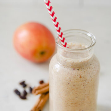 Closeup of a vintage milk bottle with apple smoothie in it and ingredients around it.