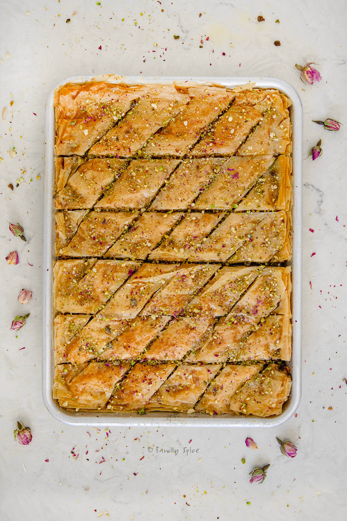 Top view of a pan of freshly baked Persian baghlava (baklava) garnished with pistachios and rose petals.