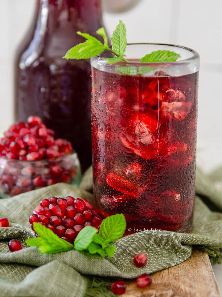 Closeup of a tall glass filled pomegranate iced tea with pomegranate arils around it.