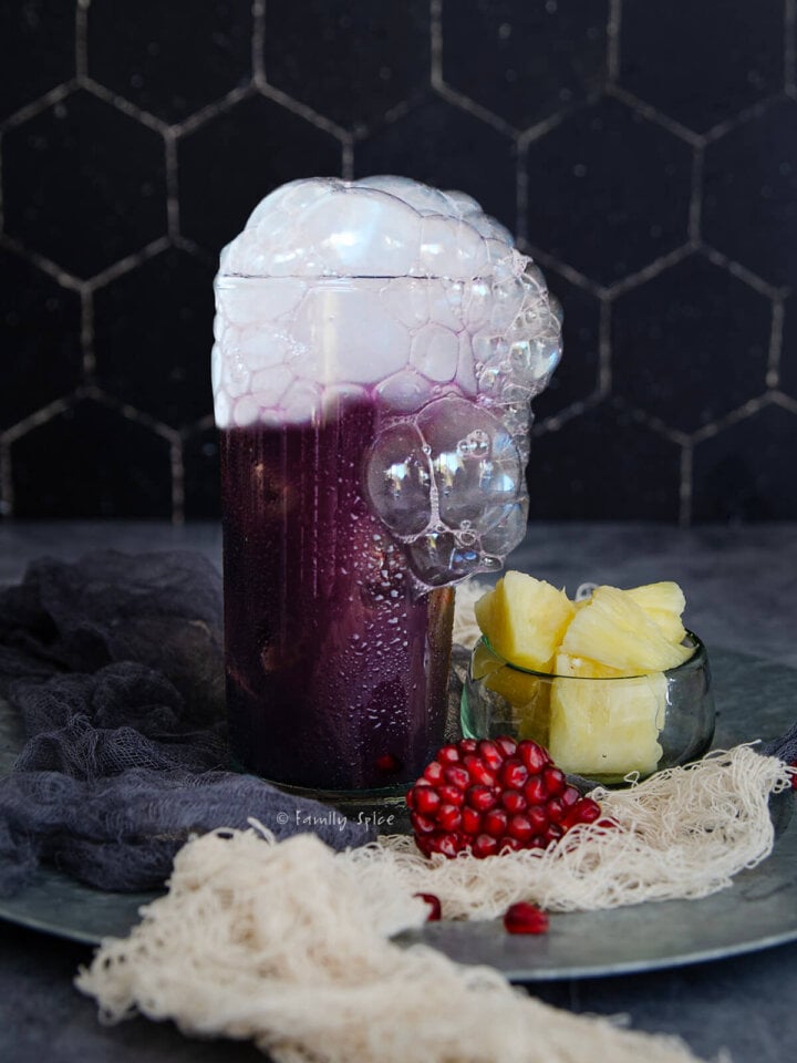 A purple cocktail in a tall glass with dry ice bubbling in it on a dark spooky background for halloween.