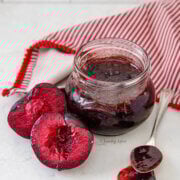 A jar of plum jam with a spoon of jam and more plums next to it.