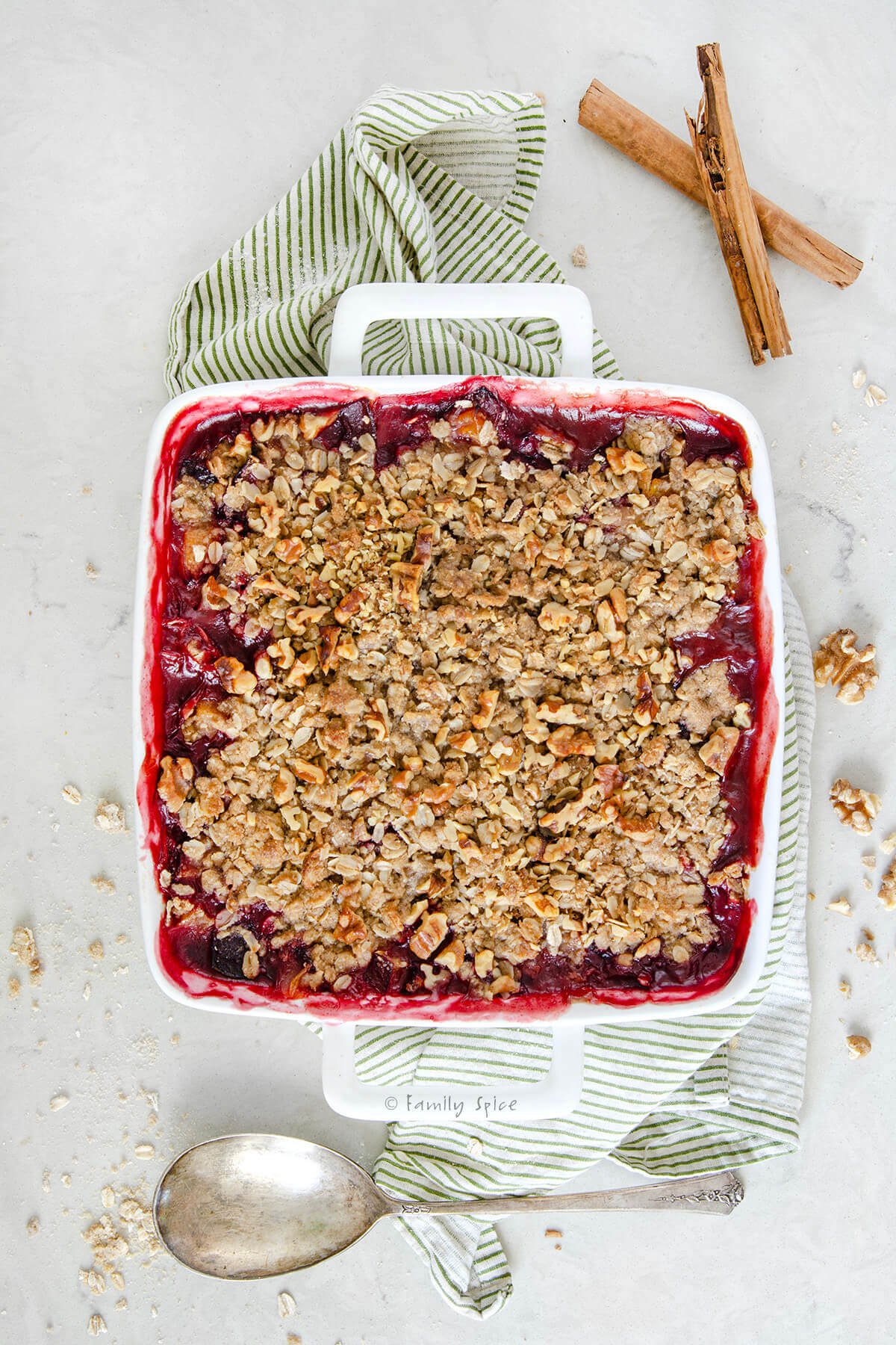 A freshly baked plum crisp with a serving spoon and cinnamon sticks next to it.