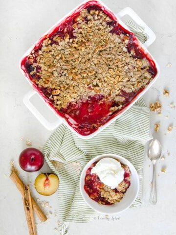 A freshly baked plum crisp with a small bowl with a single serving in it topped with vanilla ice cream.