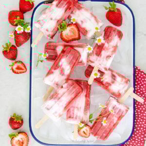 Top view of strawberry rhubarb creamsicles on a tray of ice with strawberries and flowers.