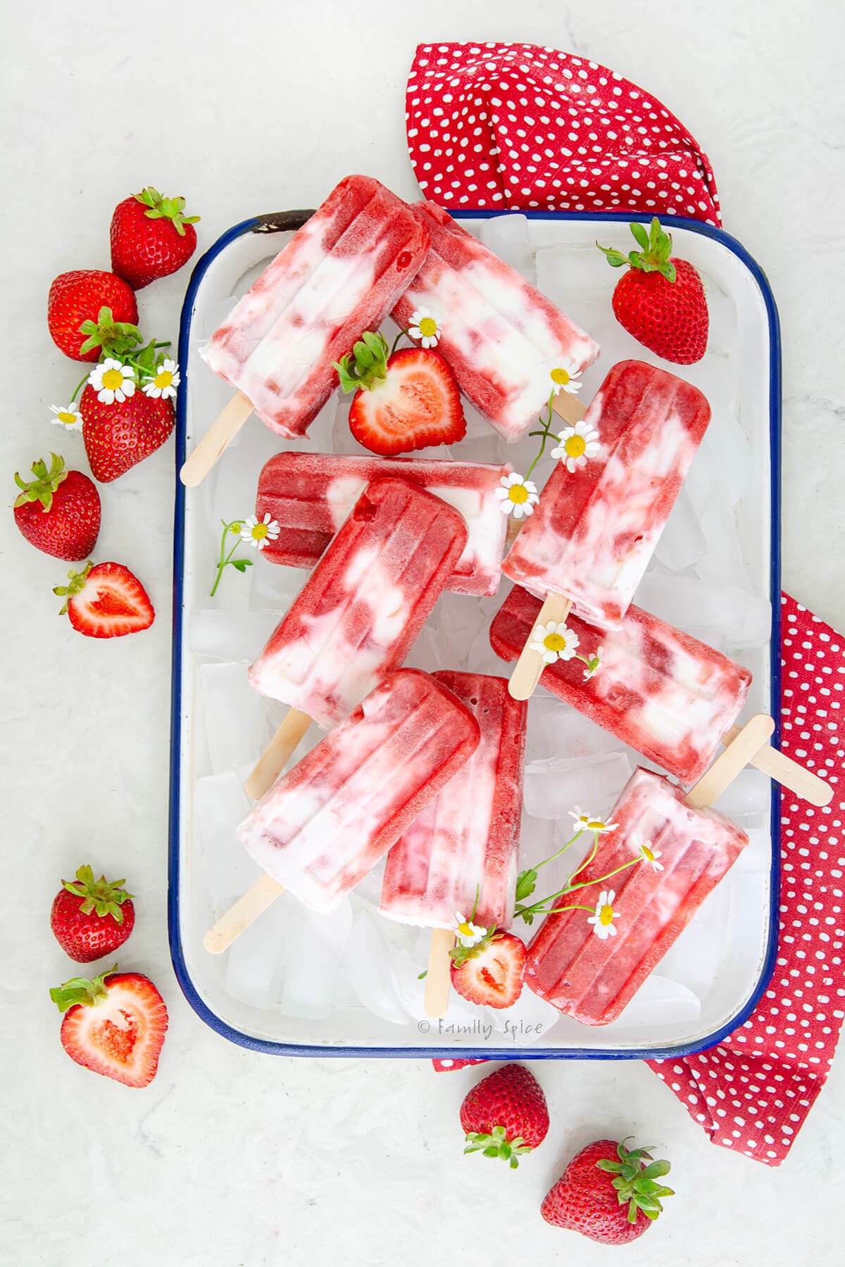 Top view of strawberry rhubarb creamsicles on a tray of ice with strawberries and flowers.