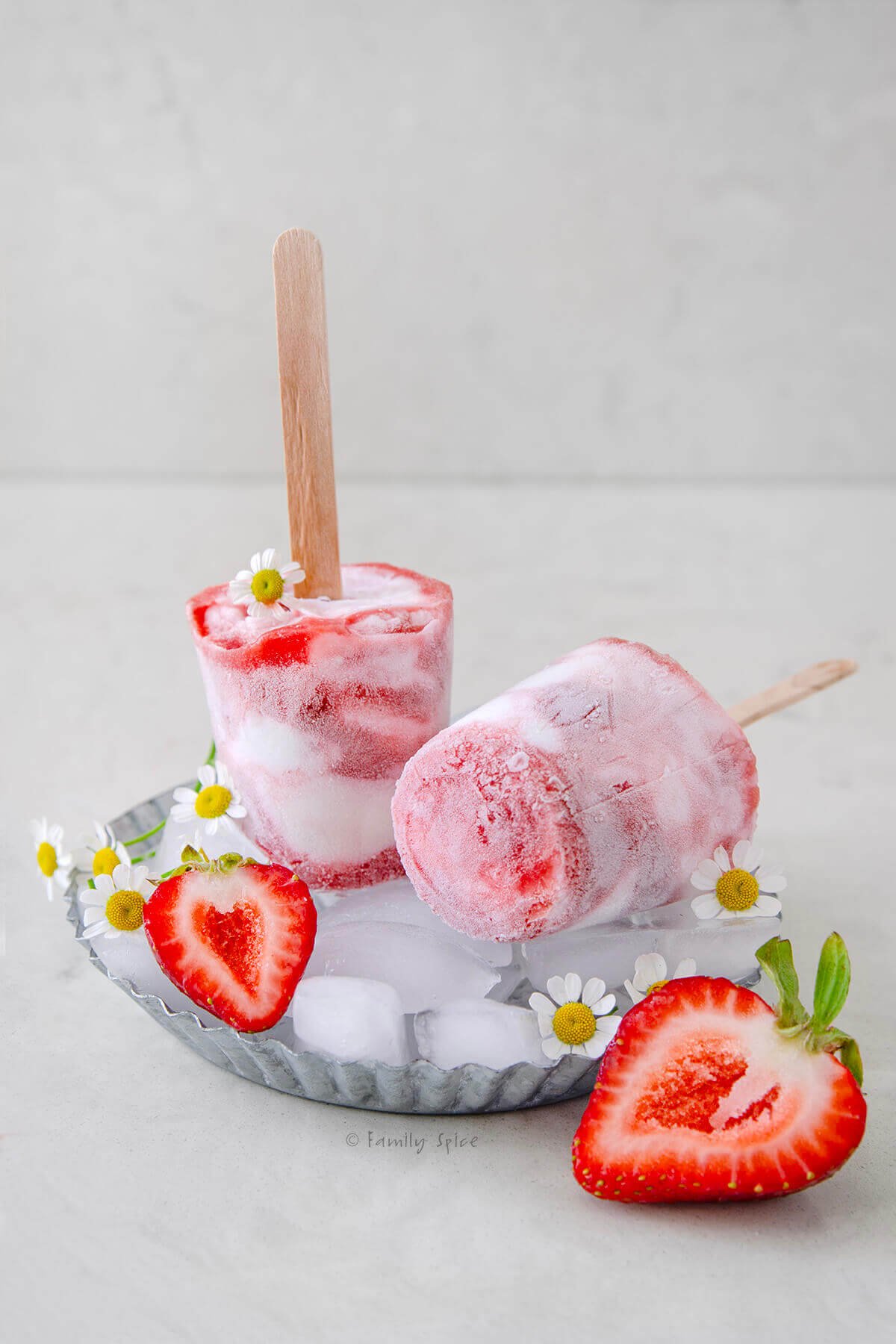 Two strawberry rhubarb creamsicles made from disposable cups on ice cubes in a metal plate.