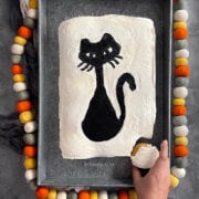 A hand pulling out one cupcake from a halloween pull apart cupcake cake frosted white with a black cat.