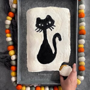 A hand pulling out one cupcake from a halloween pull apart cupcake cake frosted white with a black cat.
