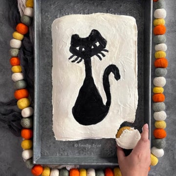 A hand pulling out one cupcake from a halloween pull apart cupcake cake frosted white with a black cat.