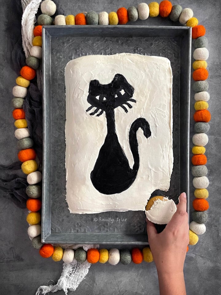 A hand pulling out one cupcake from a halloween pull apart cupcake cake frosted white with a black cat.
