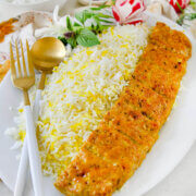Side view of a plate of rice with chicken koobideh kabob along with yogurt, herbs and radishes behind it.