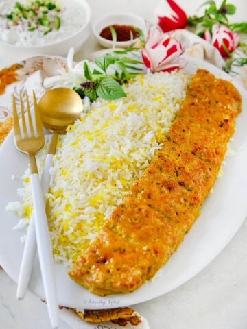 Side view of a plate of rice with chicken koobideh kabob along with yogurt, herbs and radishes behind it.
