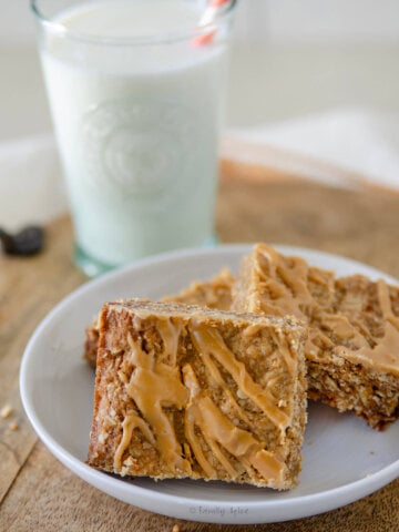 Closeup of butterscotch bars on a plate with a glass of milk behind it.