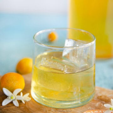 Closeup of a glass with kumquat liqueur with a bottle with more behind it.