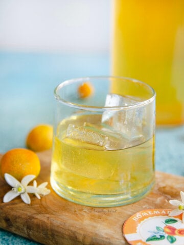 Closeup of a glass with kumquat liqueur with a bottle with more behind it.