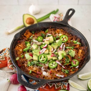 Side view of pulled pork enchilada skillet with various ingredients around it.