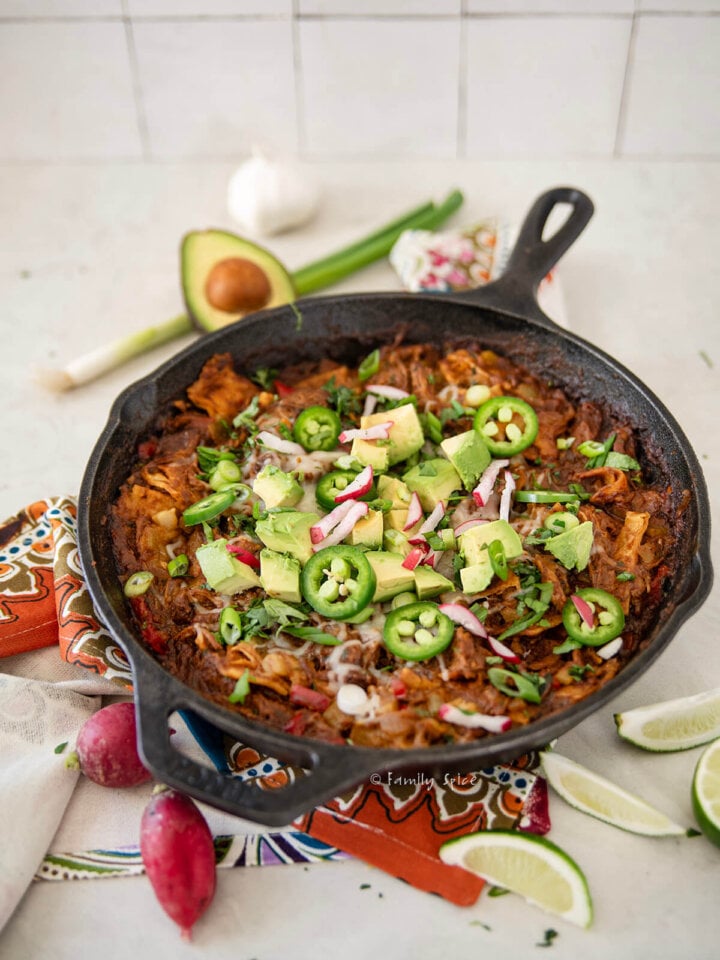 Side view of pulled pork enchilada skillet with various ingredients around it.