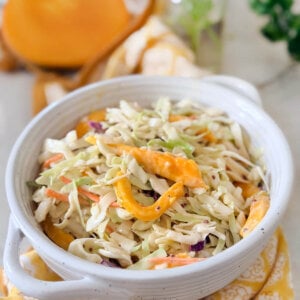 Closeup of a white bowl holding coleslaw with mango, with half a mango behind it.