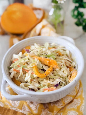 Closeup of a white bowl holding coleslaw with mango, with half a mango behind it.